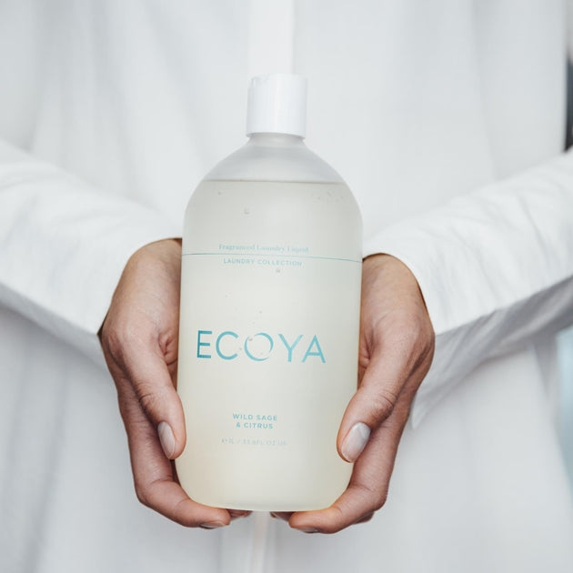 Person in a white robe holding a 1 litre bottle of Ecoya laundry liquid in both hands