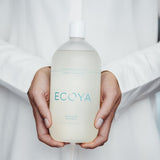 A woman holding a bottle of Ecoya Fragranced Laundry Liquid 1L, a Scandinavian-inspired fragrance gift.
