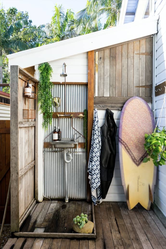 Photo from the book of an outdoor shower with wetsuits and a fish surfboard