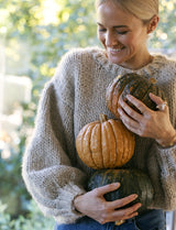 Sophie Steevens, a woman passionate about Simple Wholefoods, poses in a cozy sweater while holding pumpkins.