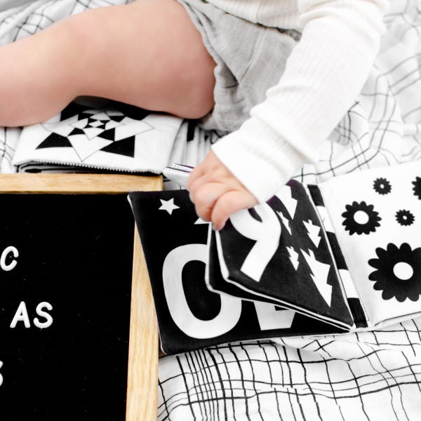 A baby is playing with a My Numbers | Luxe Soft Cover Book featuring high contrast images to help with learning numbers, made by My Family Book.