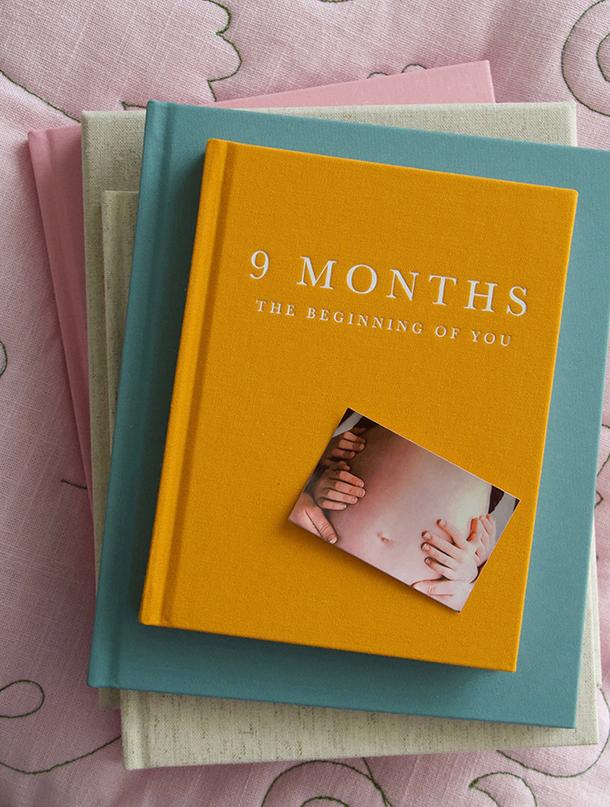 Orange 9 Months pregnancy journal with a bump photo on top, on a stack of linen journals