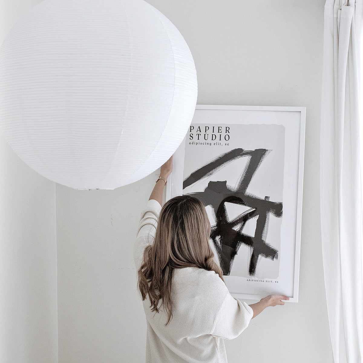 Woman hanging the framed Abstract Studio print beside a large paper globe lamp