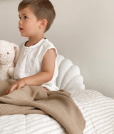 A young boy sitting on a bed with a Bengali Collections' CLASSIC KNIT BLANKET - KHAKI.