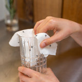 A person using a Good Change reusable bamboo towel to clean a glass with water.
