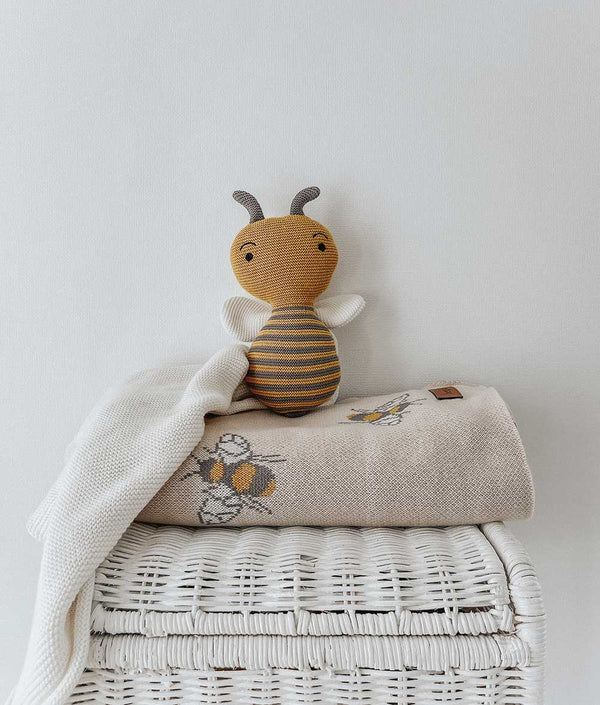 A HONEYBEE SNUGGLY made by Bengali Collections sits on top of a wicker basket.