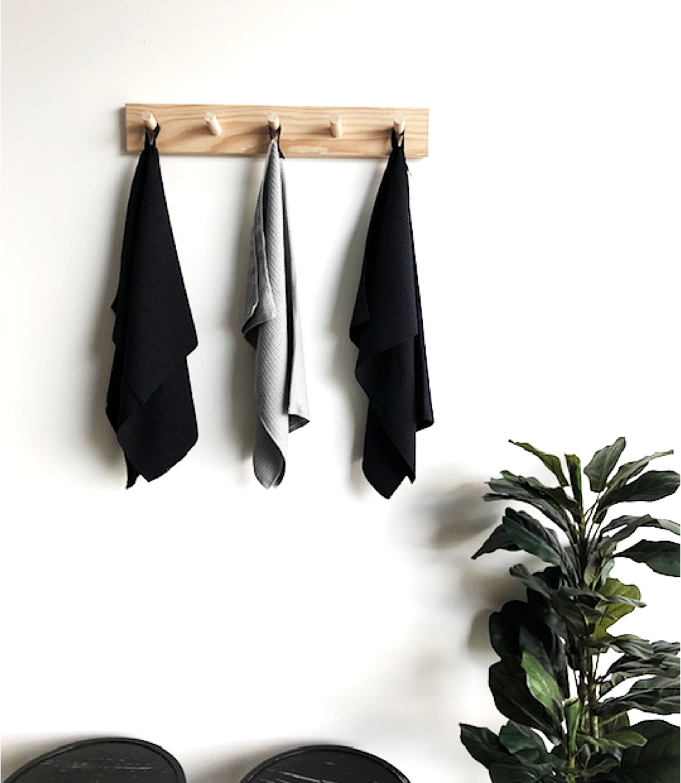 Black and grey Barkly Basics microfibre cloths hanging on a peg rail beside a plant