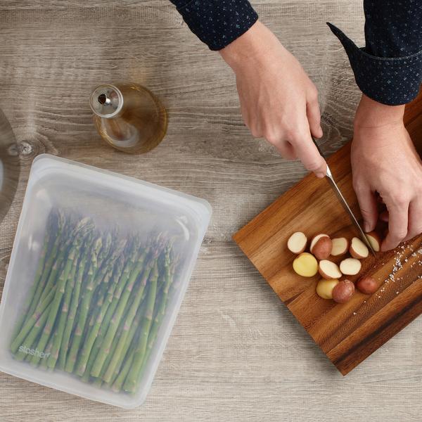 A person cutting asparagus on a cutting board using Stasher, the HALF GALLON BAG - CLEAR known for its airtight seal.