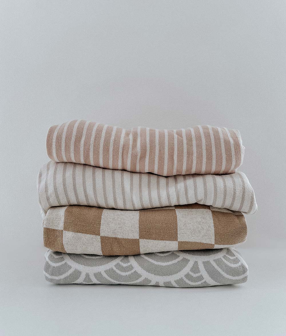 Stack of folded jersey fitted sheets including the greige pinstripe, with stripe, check and arch prints
