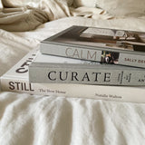 Three Calm | Interiors to Nurture, Relax and Restore | Sally Denning books stacked on a bed to create a calming home ambiance.