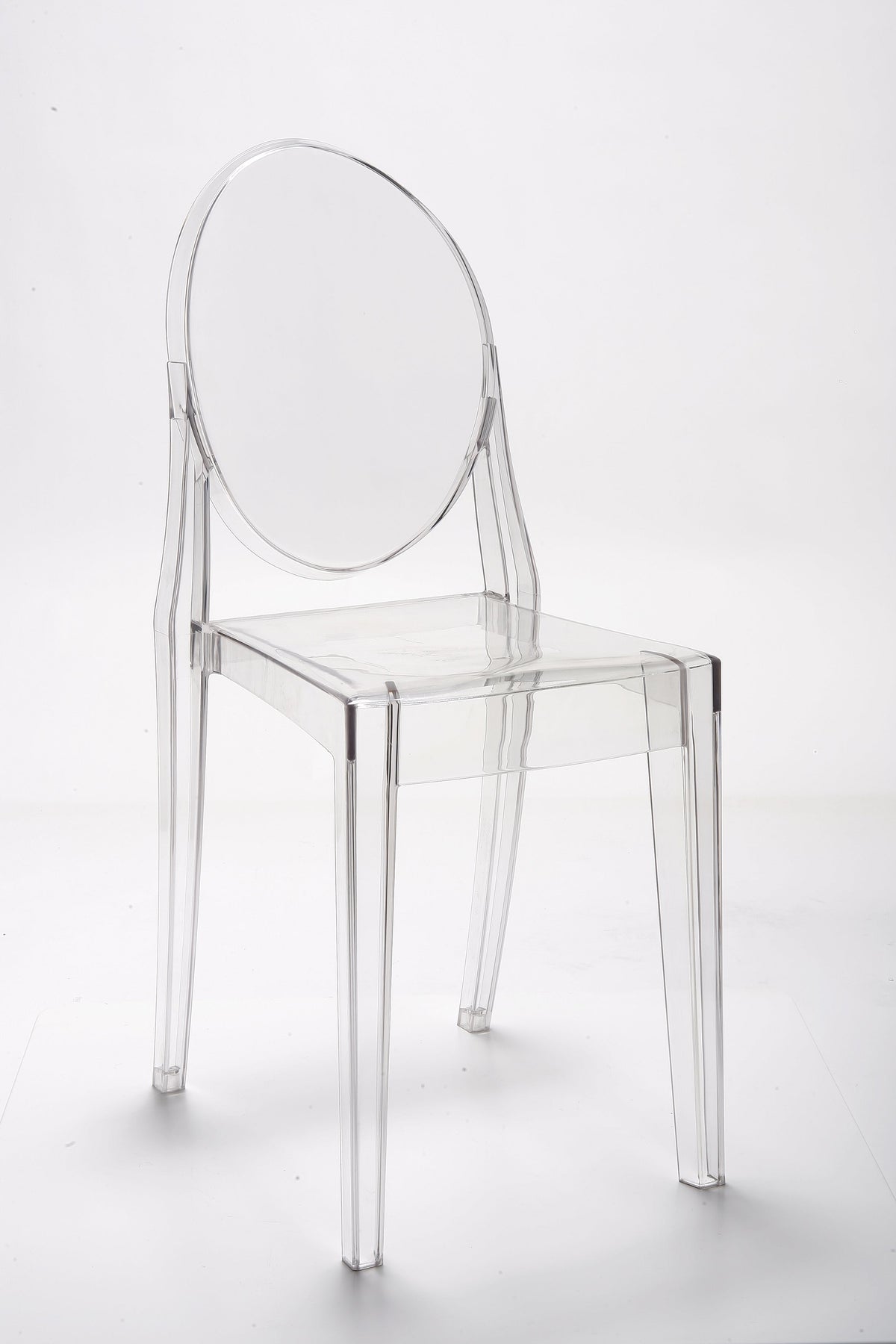 Clear acrylic dining chair seen from the front, tapered legs and oval back against a pale studio wall