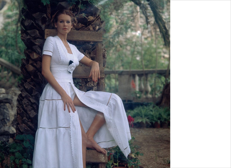 A woman is posing with Chanel: The Karl Lagerfeld Campaigns book in a white dress.