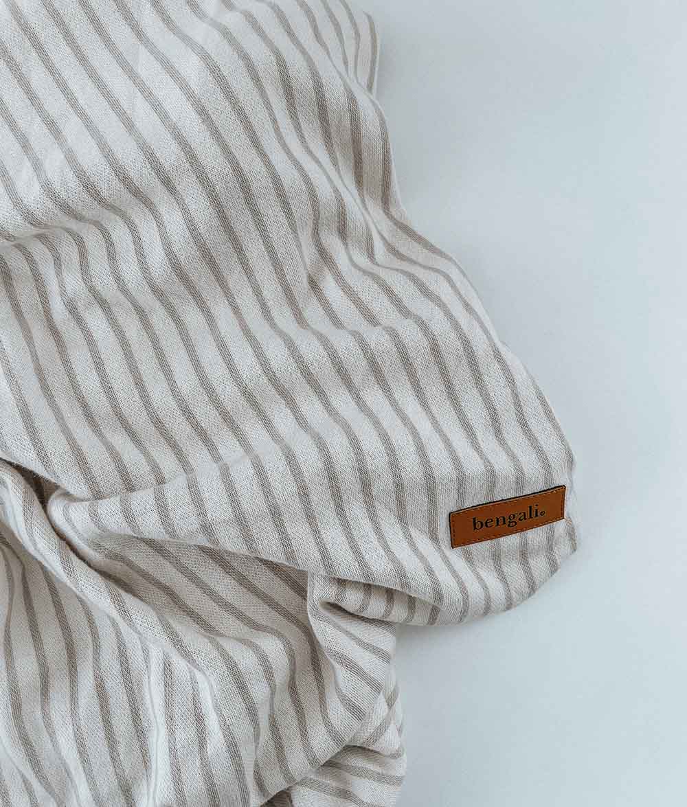 Greige pinstripe jersey fitted sheet gathered loosely, showing its leather Bengali label