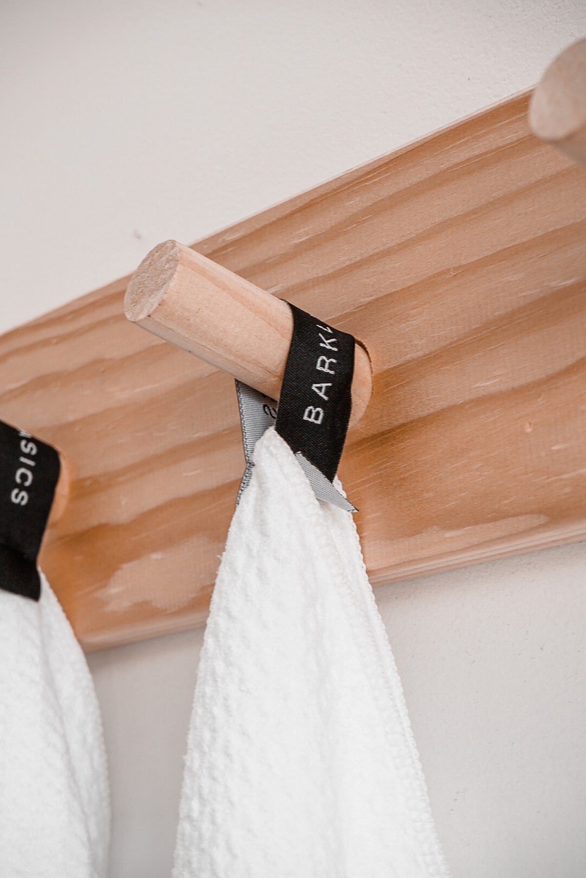 Two white waffle tea towels hanging from a timber peg rail by their Barkly Basics tags