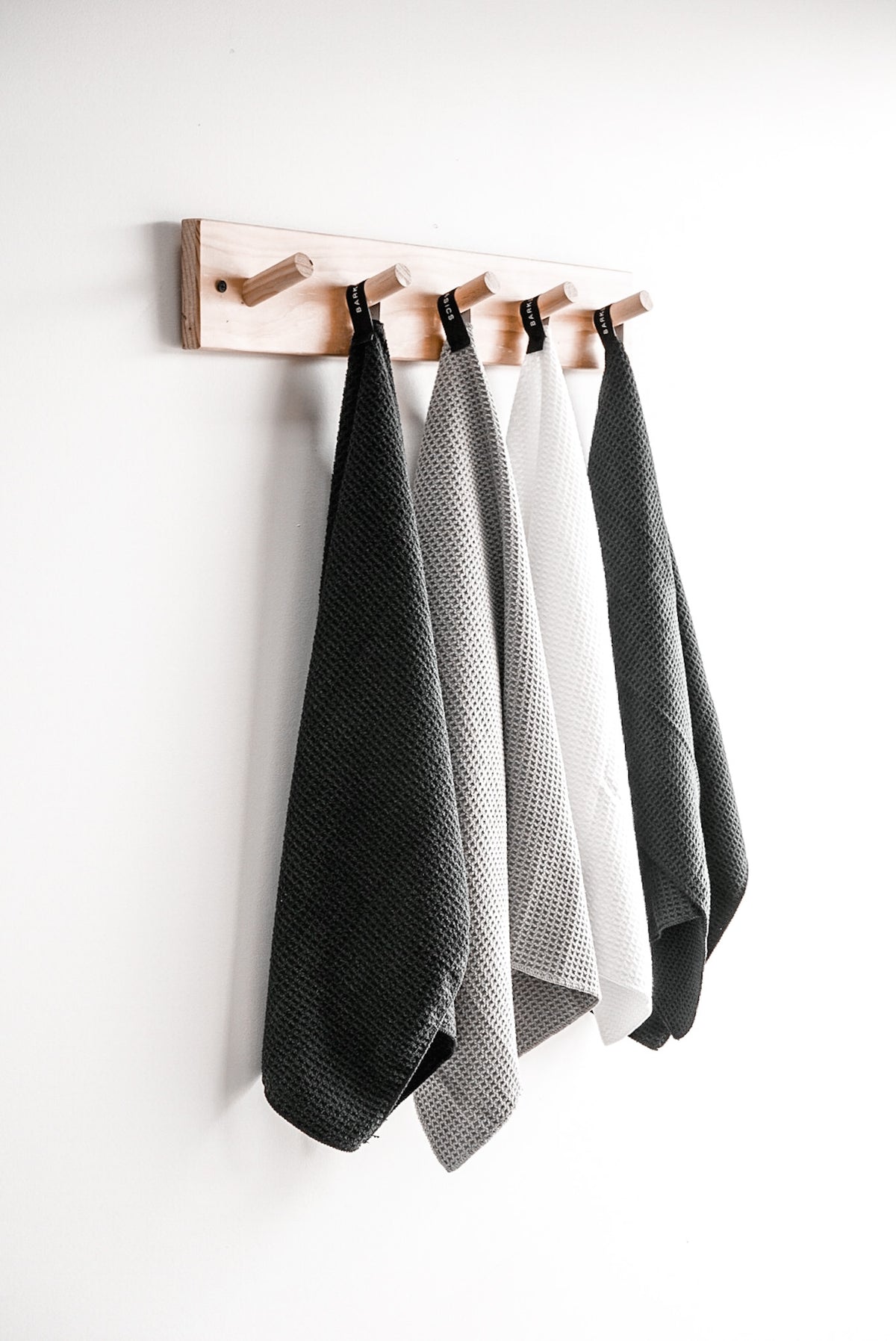 Charcoal, grey and white microfibre towels hanging in a row from a timber peg rail