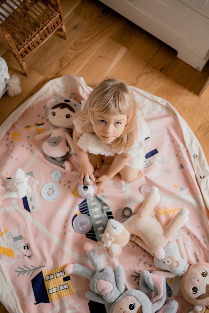 A little girl engaging in interactive play with Raindrops Village - Interactive stuffed animals from the Play Pouch range on a rug.