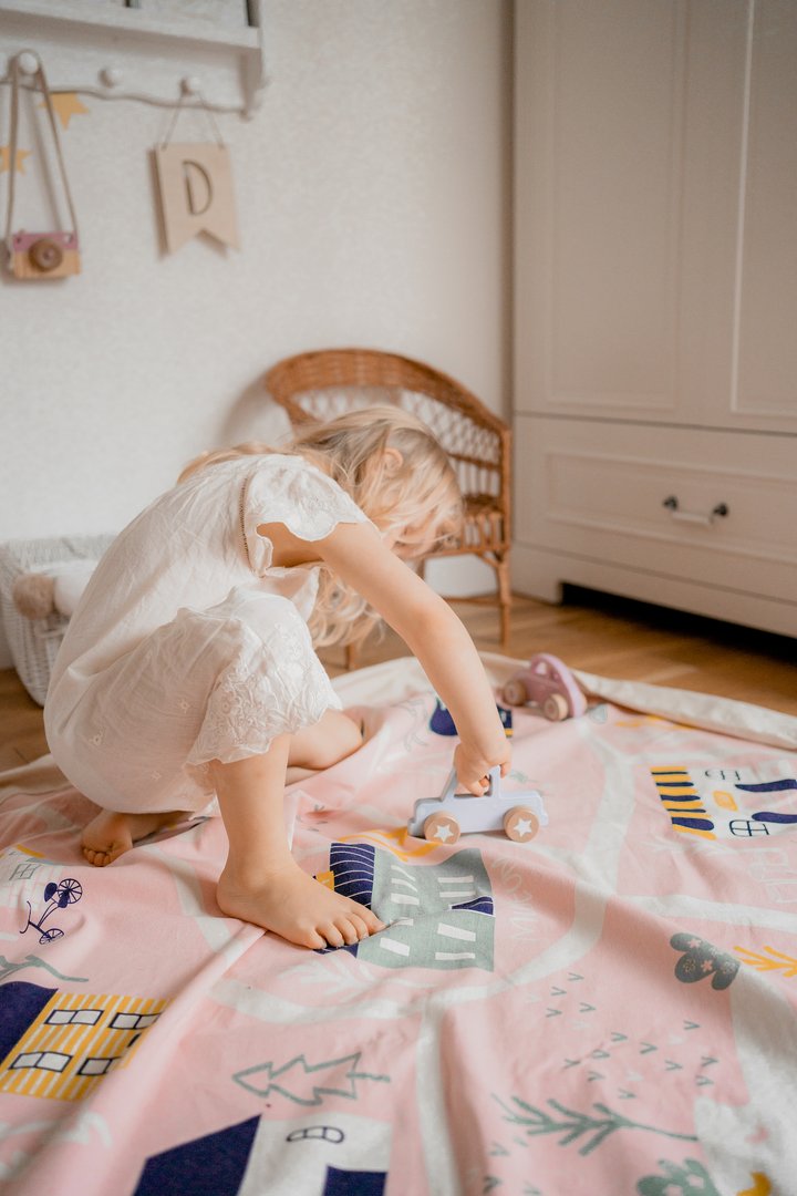 A little girl engaging in interactive play with toys on a pink rug from the Raindrops Village - Interactive range from Play Pouch.