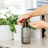 A person is placing a bottle of Ecoya Fragranced Hand Sanitizer on a Scandinavian-inspired counter.