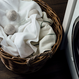 A basket full of towels in front of an Ecoya Laundry | Linen Spray, a perfect home fragrance gift.