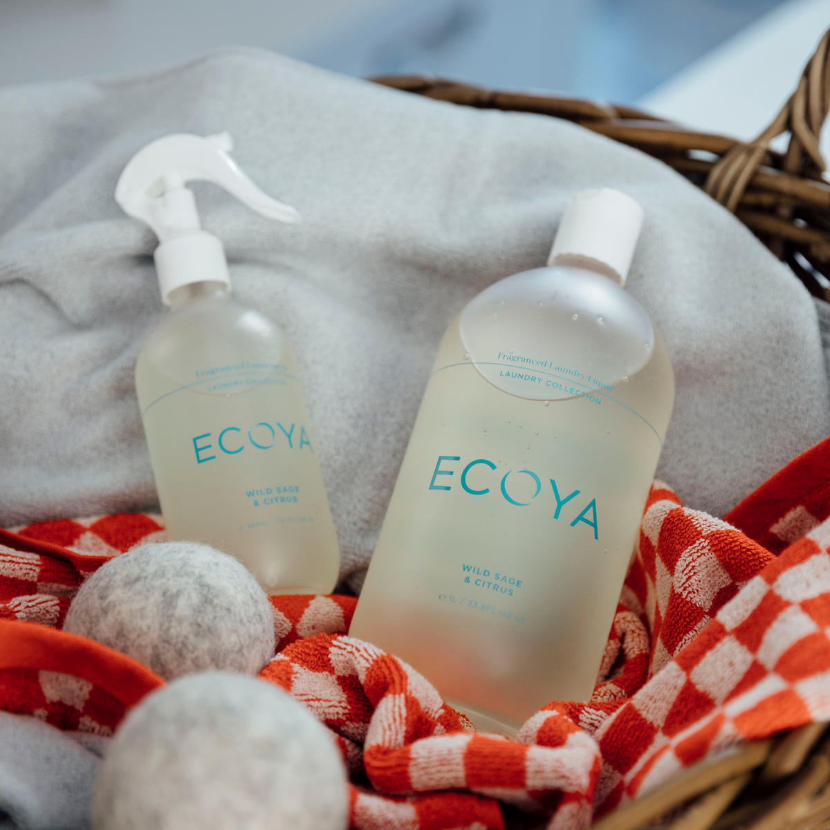 Ecoya linen spray and laundry liquid in a basket with wool dryer balls and a red gingham cloth