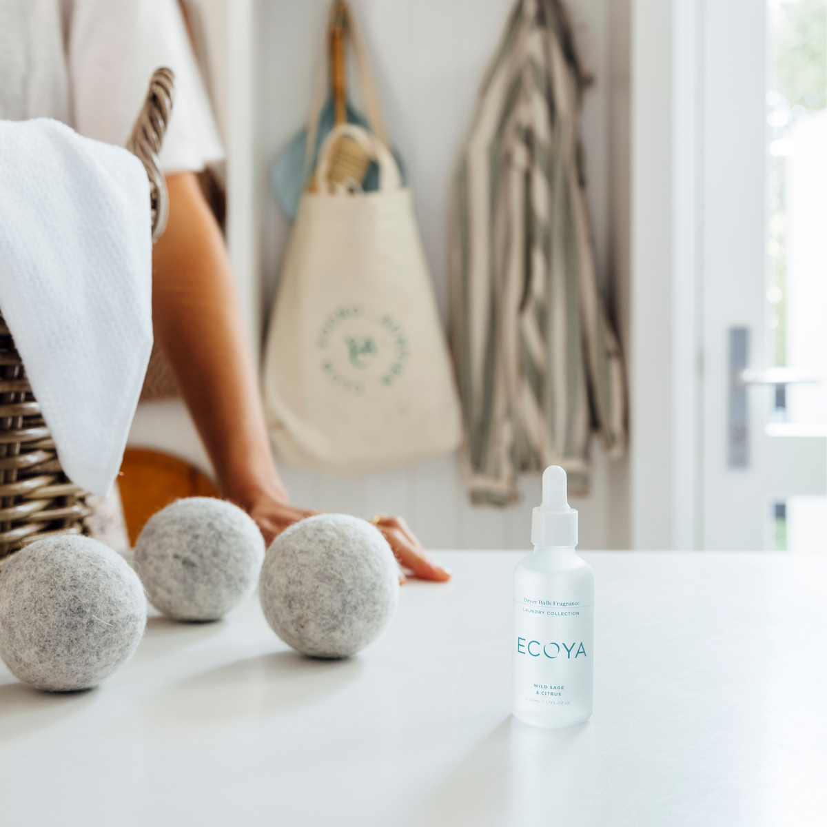 Woman at a white laundry bench with an Ecoya fragrance dropper and wool dryer balls