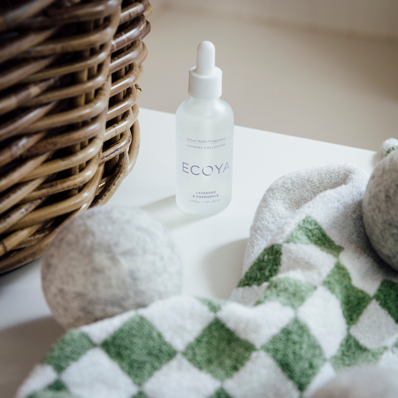 A bottle of Ecoya Laundry Fragrance Dropper on a table next to a basket of towels, creating a scandinavian-inspired home fragrance.