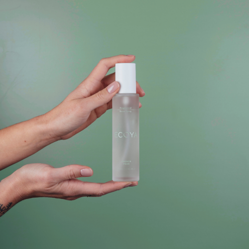 A person holding a fragranced room spray bottle on a green background, perfect for home fragrance or gifting.