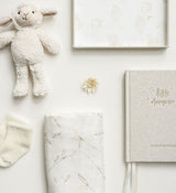 A baby's nursery with a Olive Branch Baby Swaddle, a teddy bear, a blanket and a book from Emma Kate Co.