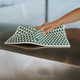 A person using a Good Change eco cloth to clean a metal counter in a sustainable manner.