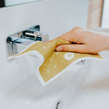 A person cleaning a sink with a yellow cloth, using Good Change ECO CLOTH - MEDIUM (3-PACK) for an effective and thorough clean.
