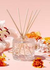 The Aromatherapy Co FLWR Diffuser - Fleur D'Oranger, with orange blossoms on a pink background.