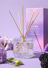 The Aromatherapy Co's FLWR Diffuser - Purple Reign on a purple background with blackberries and flowers.