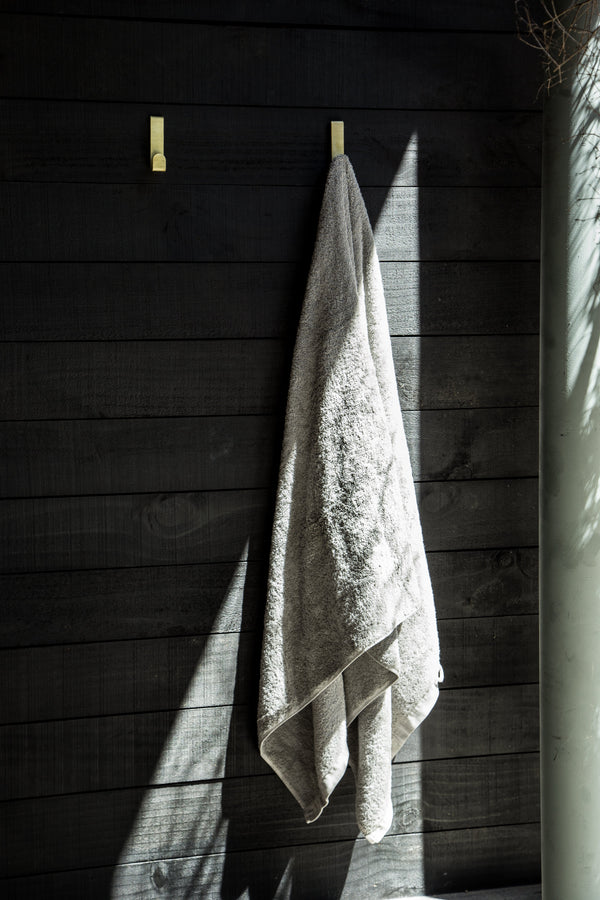 A durable Fold Loop Hook - Stainless towel hanging on a wooden wall with loop hooks, made by Made of Tomorrow.