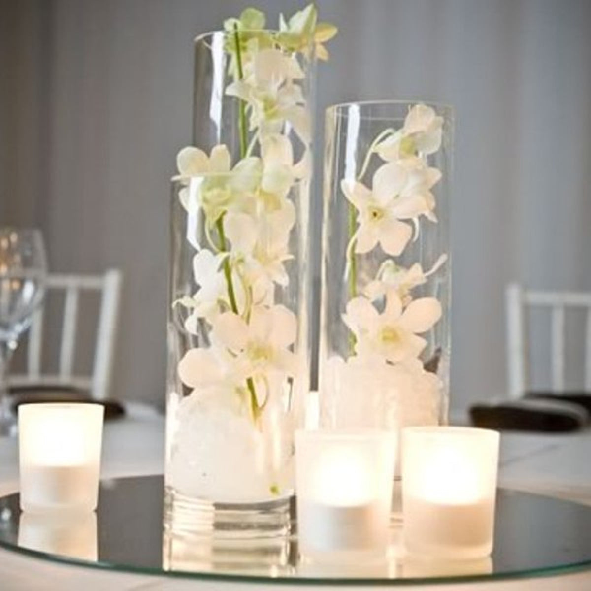 Glass cylinder vases filled with white orchids on a mirror centrepiece with tealight candles