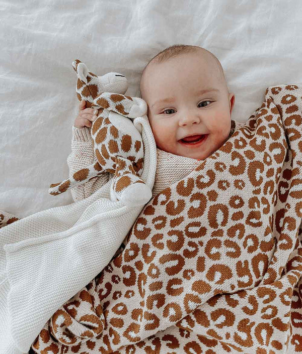 A baby laying on a bed with a Bengali Collections GIRAFFE SNUGGLY blanket.