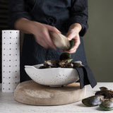 A woman pouring brightly coloured mussels into a Good Change limited edition Swedish Dish Cloths - Black (2-PACK) bowl.