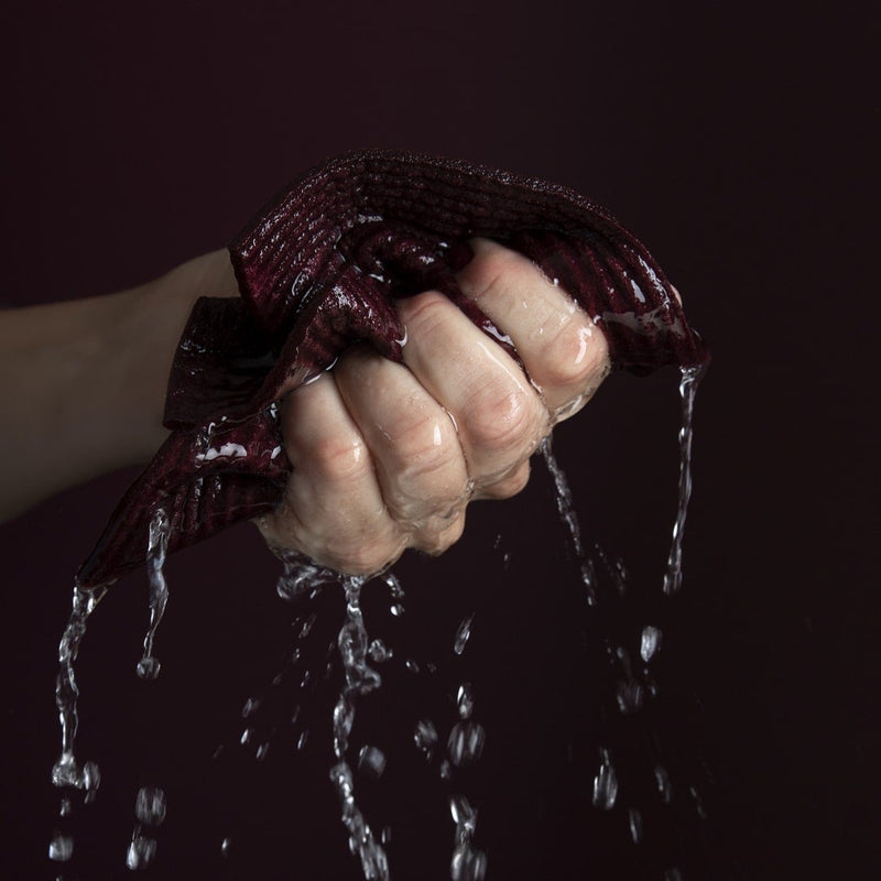 A woman holding a Good Change Swedish Dish Cloths - Black (2-PACK) with water on it.
