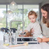 A woman and child washing dishes in a kitchen sink using the Good Change Kitchen Reusable Spray Bottle for good change.