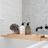 A Scandinavian-inspired bathroom with an Ecoya wooden tub tray and Fragranced Hand and Body Wash soap dispenser.