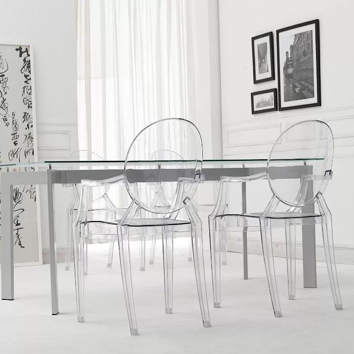 Four clear acrylic armchairs around a glass dining table, with framed artwork and sheer curtains