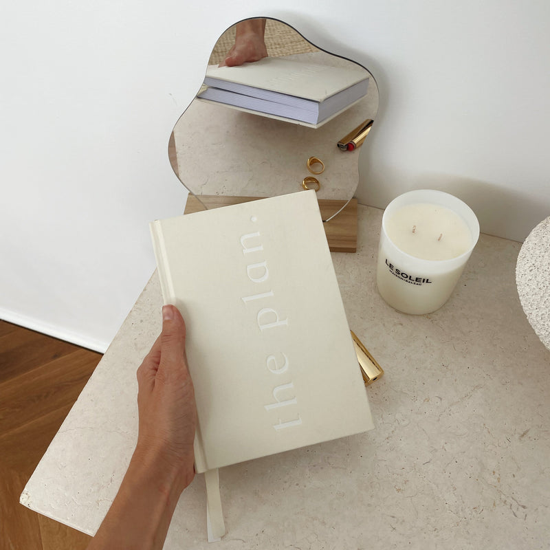 A person holding a limited edition Planner - Sand from the Papier HQ stationery range, next to a candle on a table.