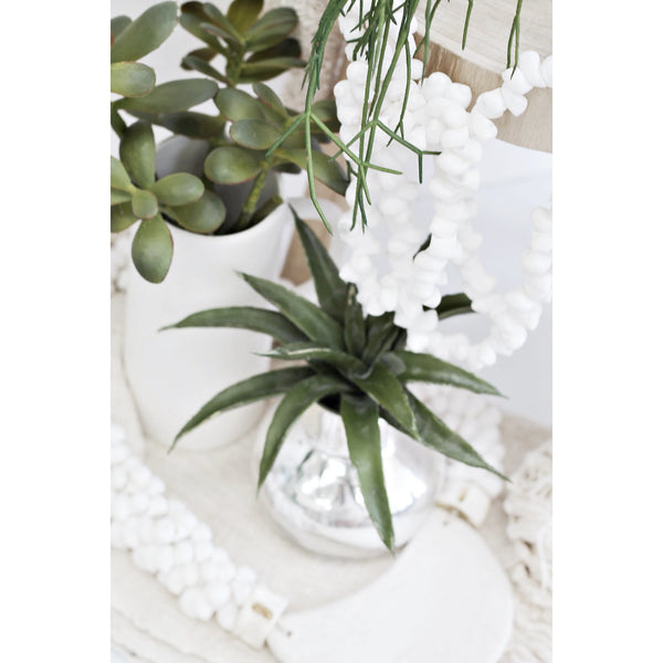 A white vase with Artificial Flora's Desert Plant and a beaded necklace.