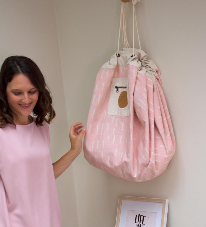 The woman in the pink dress is showcasing a Raindrops Village - Interactive from the Play Pouch range, which is conveniently stored in her pink bag.