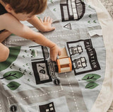 A child is engaging in imaginative play with a Play Pouch Wow Town Track Interactive on a rug.