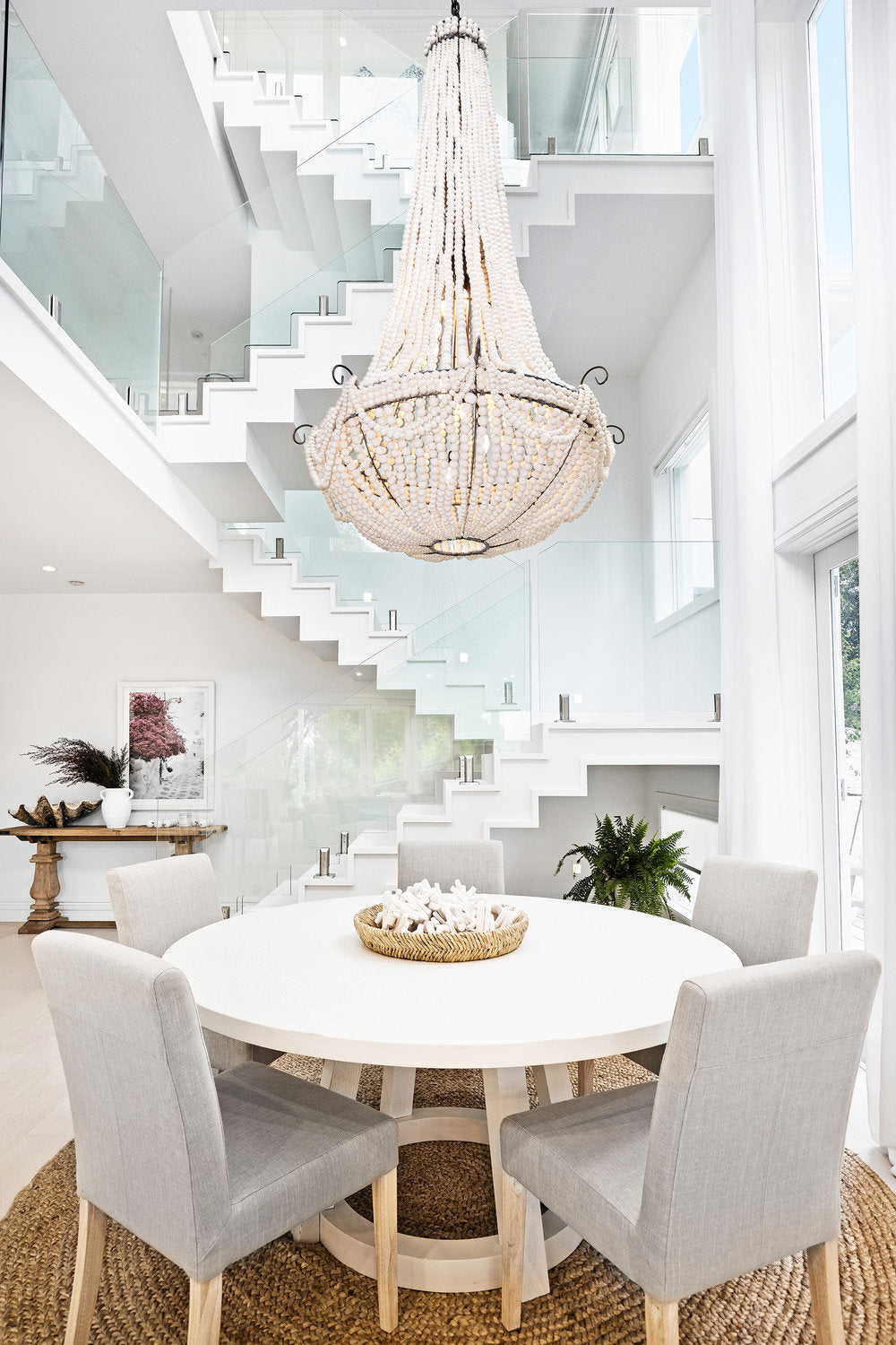 Round white dining table under a beaded chandelier beside a white staircase