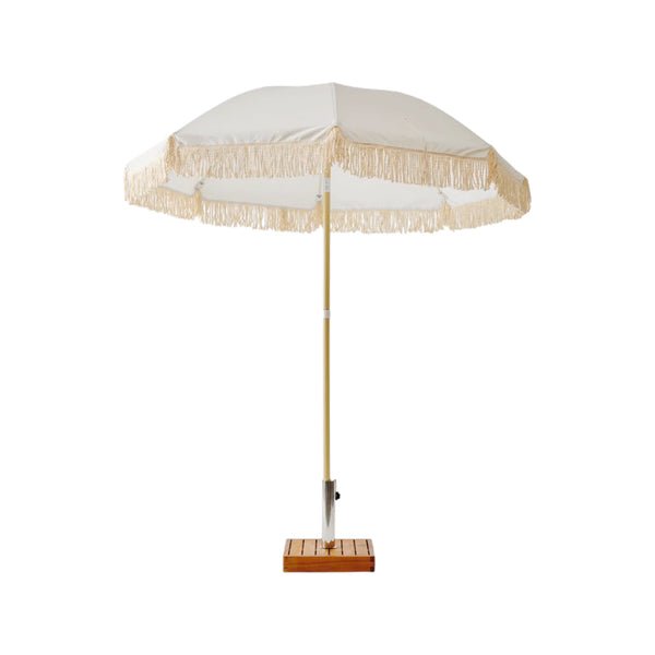 A lightweight Brel Club Fringe umbrella with tassels on a wooden stand.