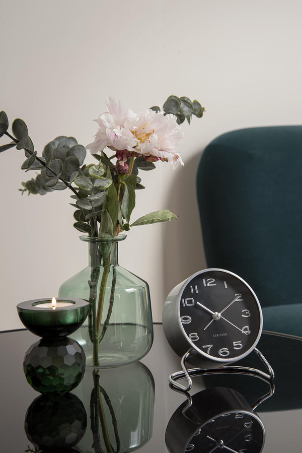 A Karlsson Classical Numbers - Silent Alarm Clock sits on a table next to a vase of flowers.