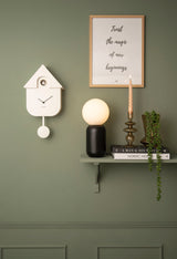 A Karlsson Modern Cuckoo - Various Colours wall clock with a plant on it.