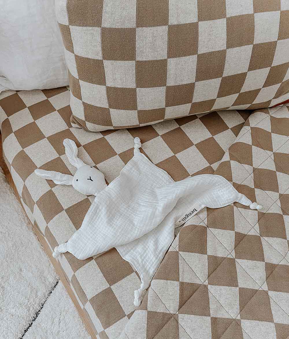 White bunny comforter lying on khaki gingham check bedding with the check pillow behind