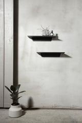 Two functional black shelves, the Made of Tomorrow FOLD Ledge 450mm ∙ White, on a wall next to a potted plant.